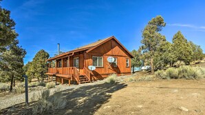 A wooden cabin with a porch, satellite dish, and a dirt driveway.