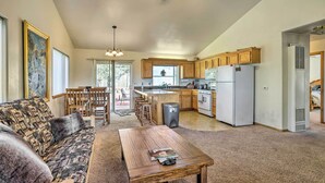 A spacious living area with a sofa, a wooden table, and a kitchen with wooden cabinets and a refrigerator.