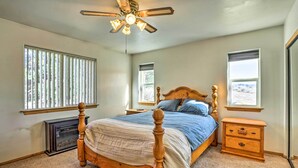 A bedroom with a wooden bed, a ceiling fan, and two windows.