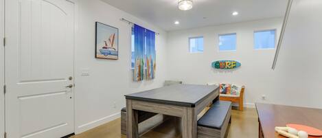 A modern, well-lit room with a white door, a table with benches, a small rug, and a surfboard decoration.