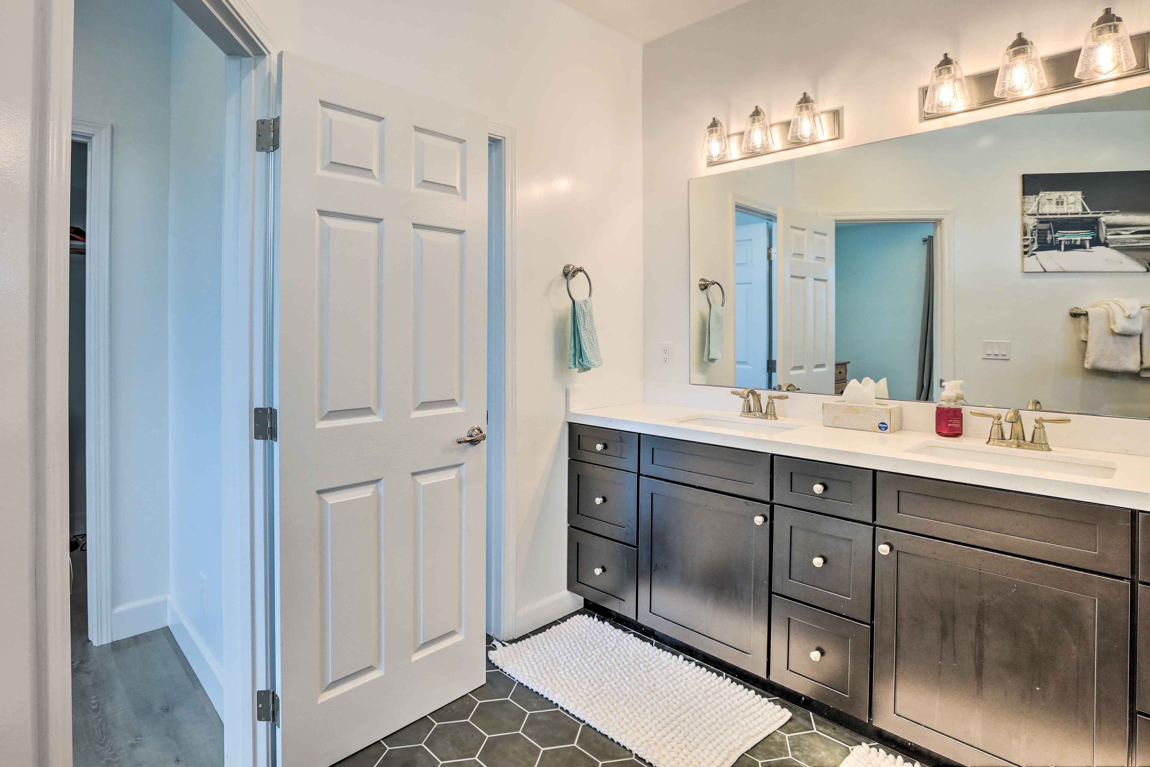 A bathroom with a white door, a large mirror, a white sink, and dark cabinets.