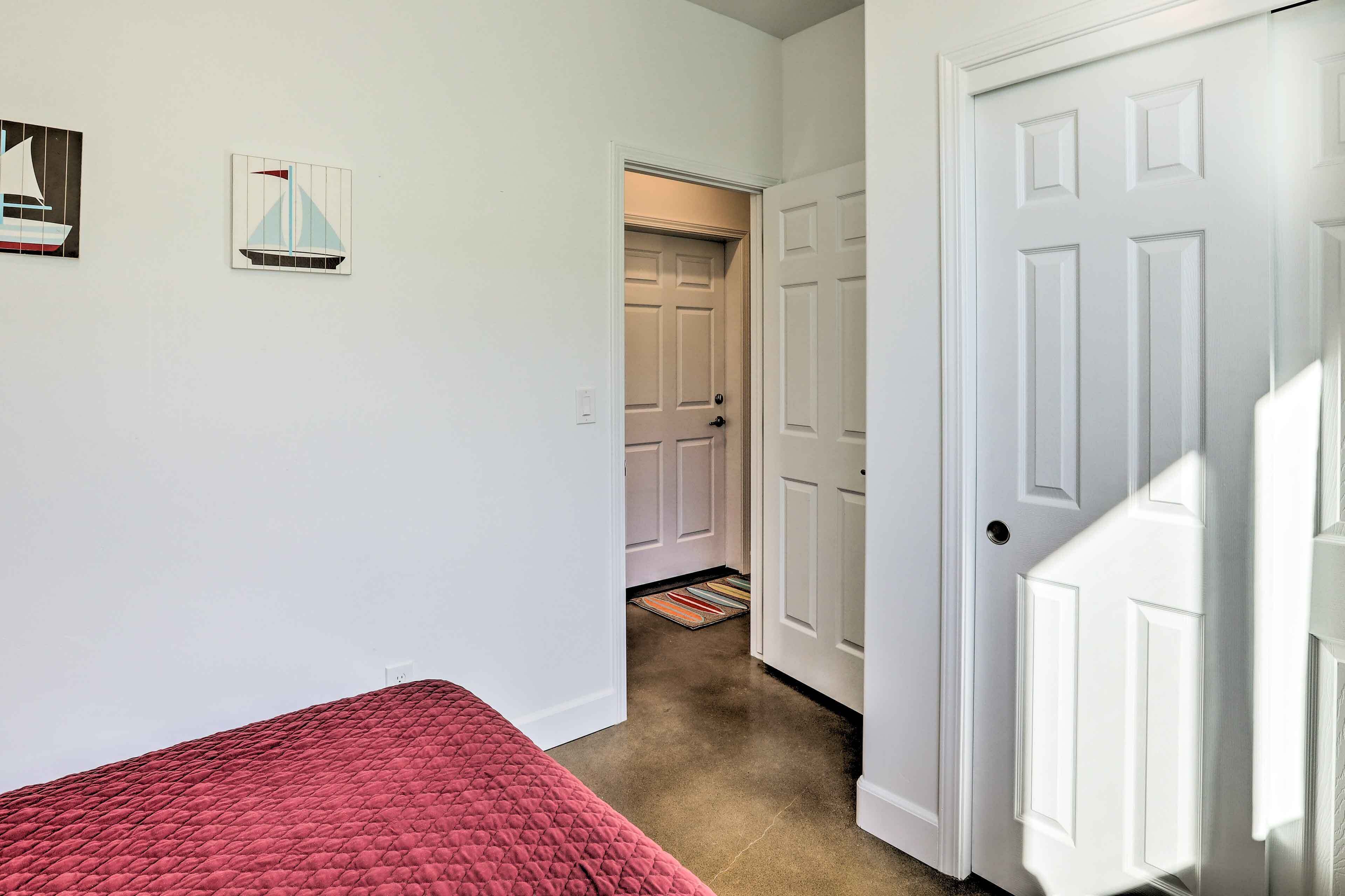 A bedroom with a red bedspread, white walls, and a door leading to another room.