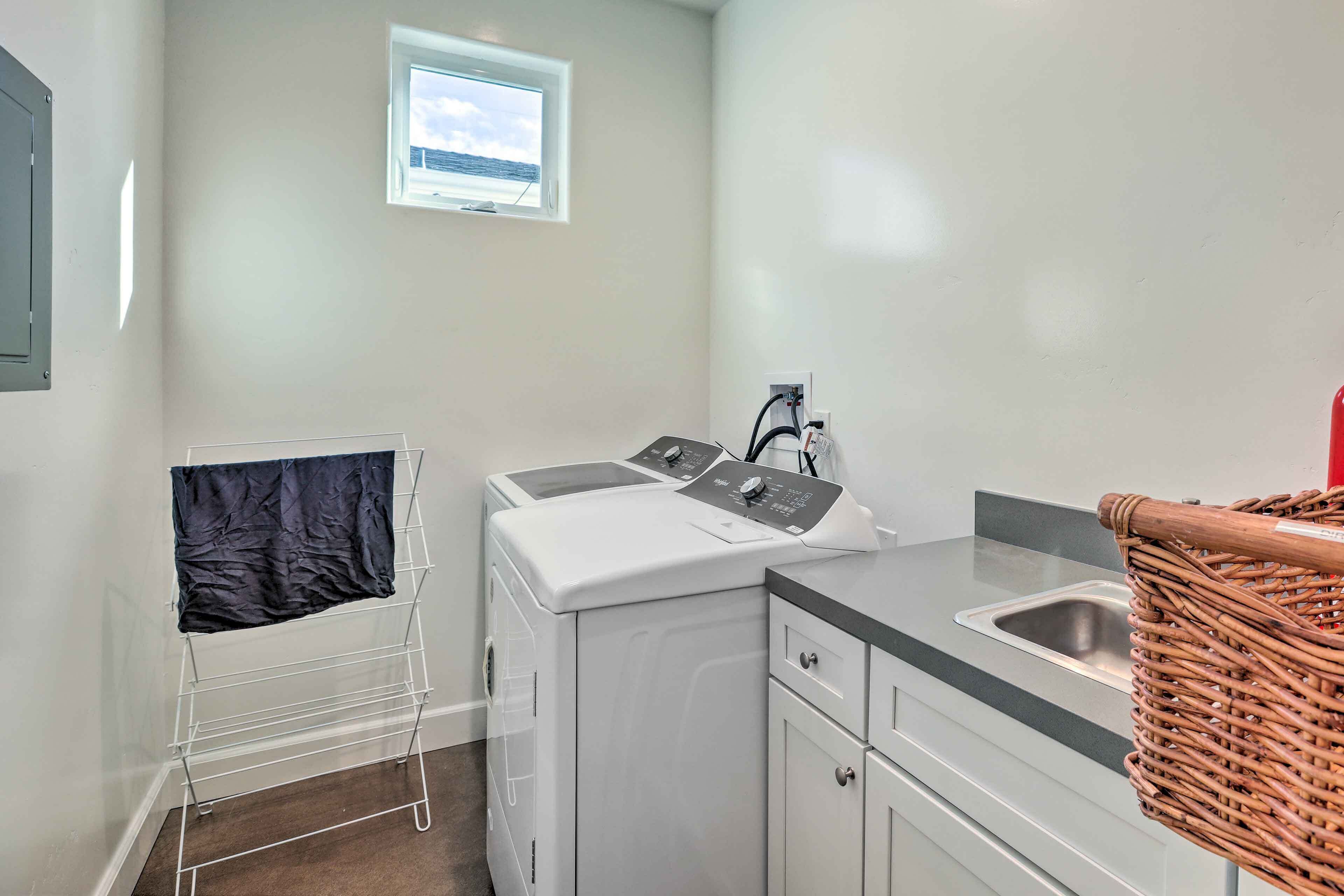 A compact laundry area with a washing machine, a drying rack, a sink, and a small window with a view.