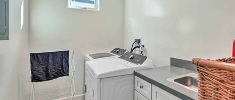 A compact laundry area with a washing machine, a drying rack, a sink, and a small window with a view.