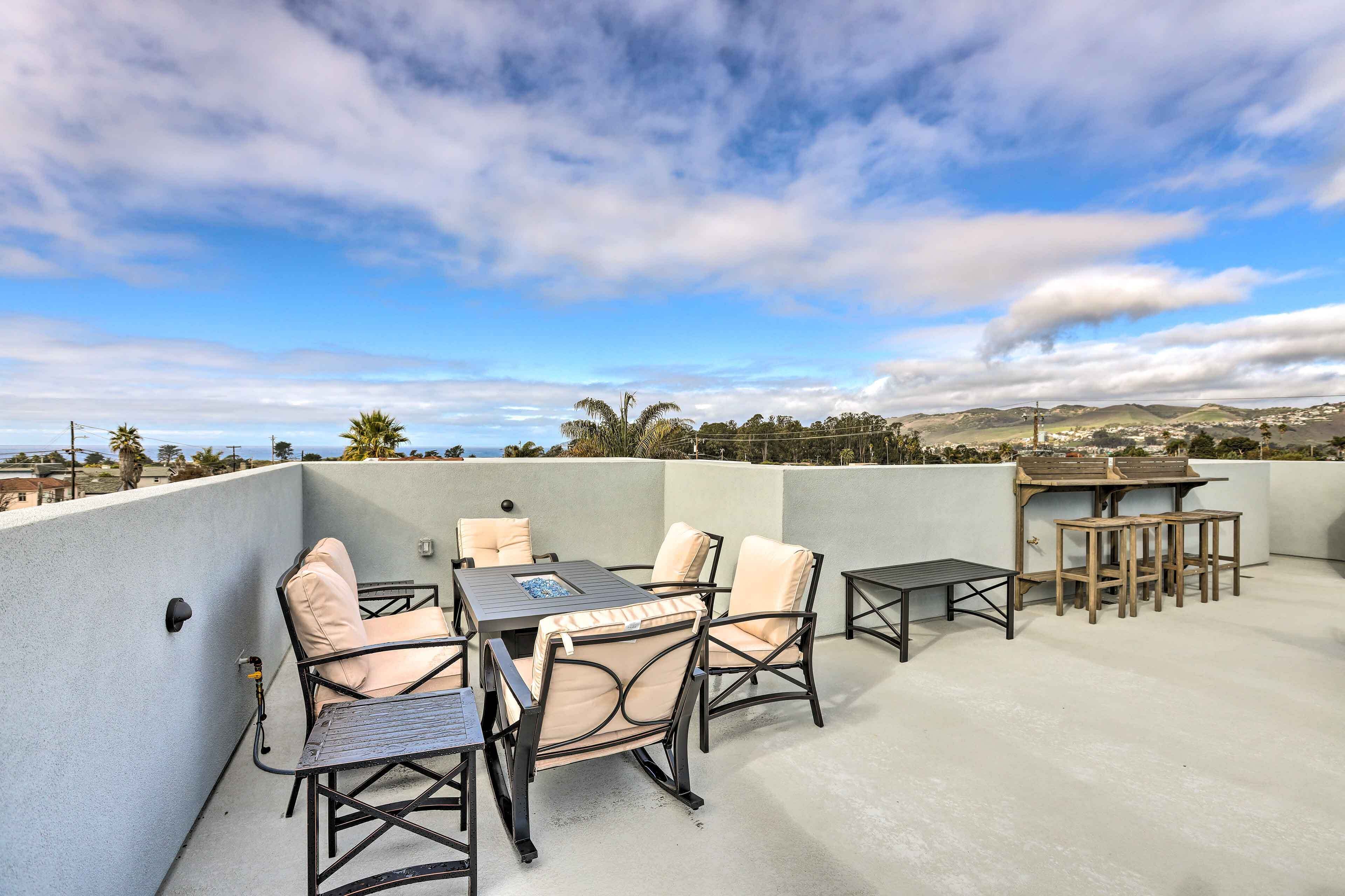 A rooftop patio with outdoor furniture, a table, and a view of the landscape.