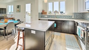 A modern kitchen with a central island, dark cabinets, and a large window. - Stunning Getaway < 1 Mi to Grover Beach! (Grover Beach)