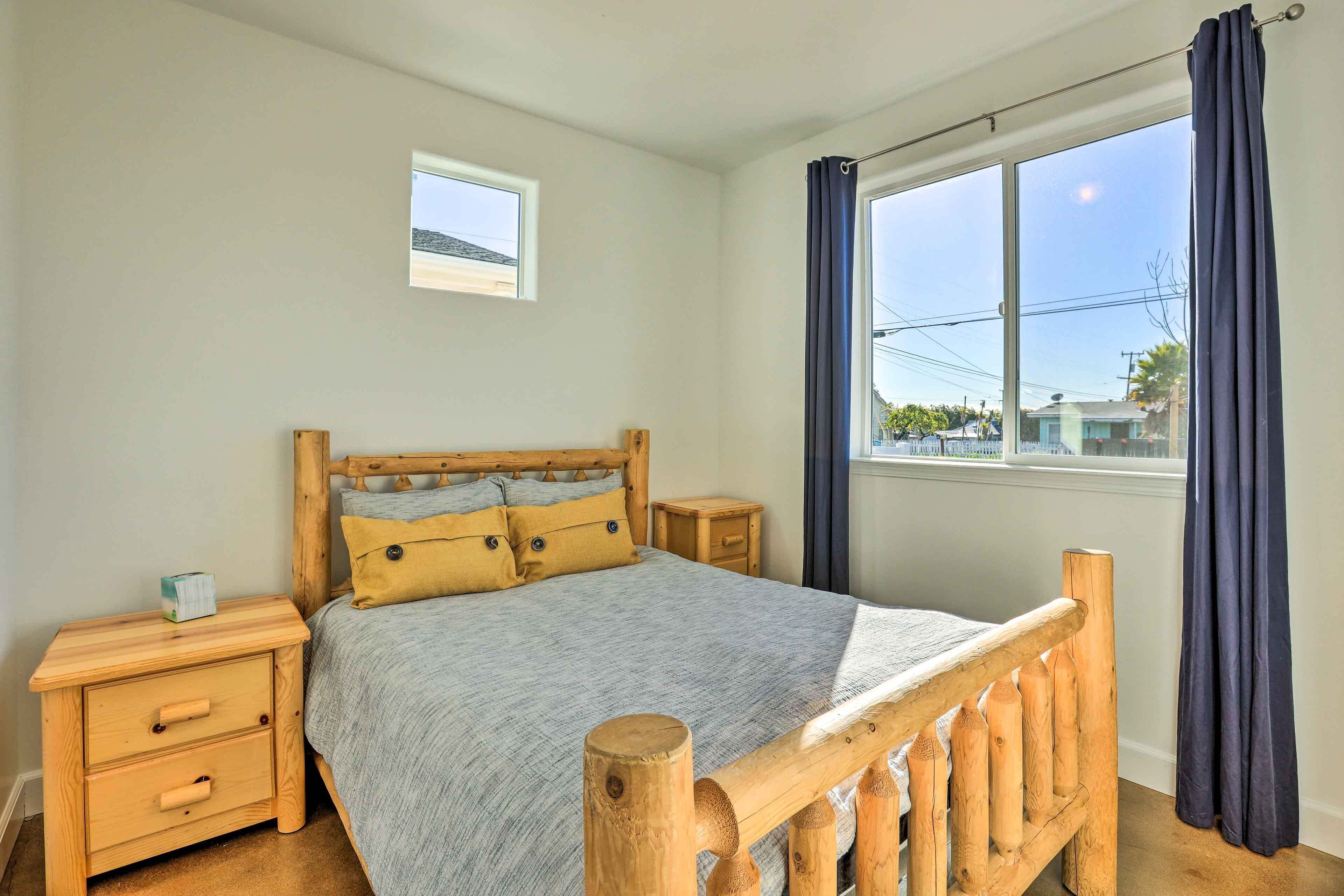A bedroom with a wooden bed, a nightstand, a small window, and a view of the outside.