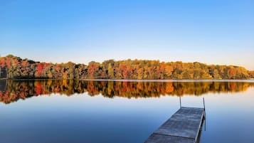 A calm lake with a dock extending into the water, surrounded by trees with autumn foliage.