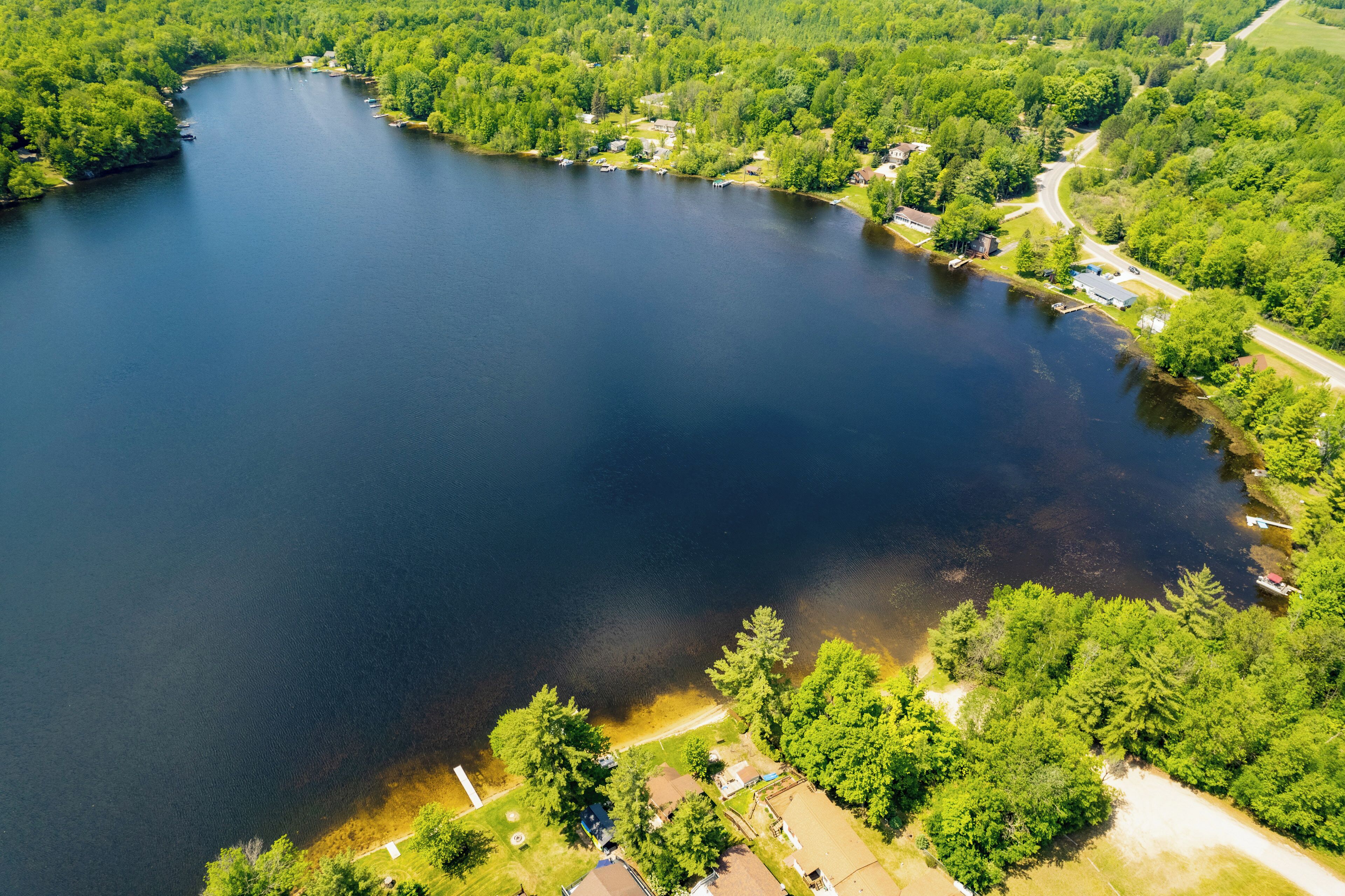 An aerial view of a lake surrounded by dense forest and residential areas with visible houses and roads.