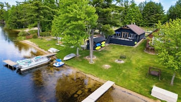 A lakeside property with a dock, boat, and a house with a deck.