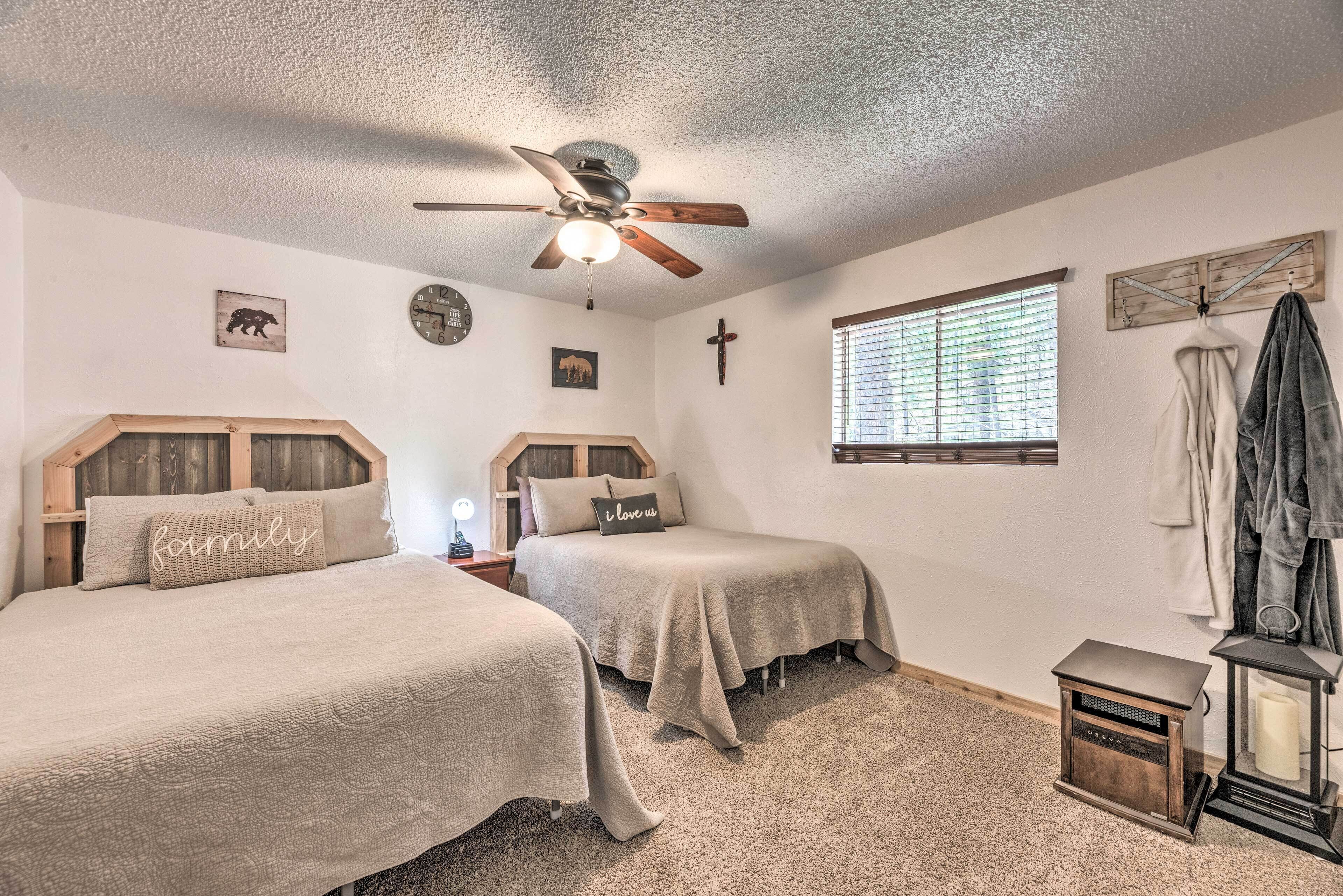A bedroom with two beds, a ceiling fan, a clock, and a window with blinds.