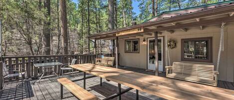 A wooden deck with picnic tables and benches, surrounded by tall pine trees.