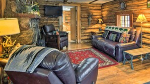 A log cabin interior with a fireplace, leather sofas, a wooden coffee table, and a television mounted on the wall. - Allenspark Vacation Rental Near Estes Park! (Allenspark)