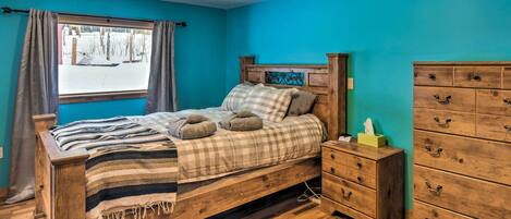 A bedroom with a wooden bed, a nightstand, a dresser, and a window with curtains.