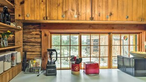 A kitchen with wooden cabinets, a window with a view of trees, a blender, a red toaster, and a microwave. - Allenspark Vacation Rental Near Estes Park! (Allenspark)