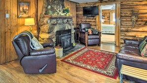 A log cabin interior with a stone fireplace, leather sofas, and a red patterned rug. - Allenspark Vacation Rental Near Estes Park! (Allenspark)