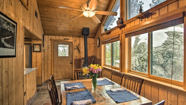 A wooden dining area with a table set for four, a ceiling fan, and a window with a view of snow-covered trees. - Allenspark Vacation Rental Near Estes Park! (Allenspark)
