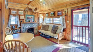 Ein gemütliches Blockhaus-Interieur mit Holzbalkendecke, Kamin, einer Couch und einem Esstisch.