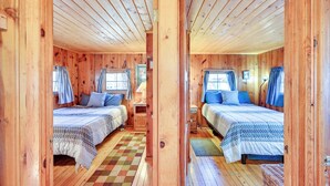 Eine Holzhütte mit zwei Betten, einem Schachbrettmuster Boden und einem Fenster mit Vorhängen.