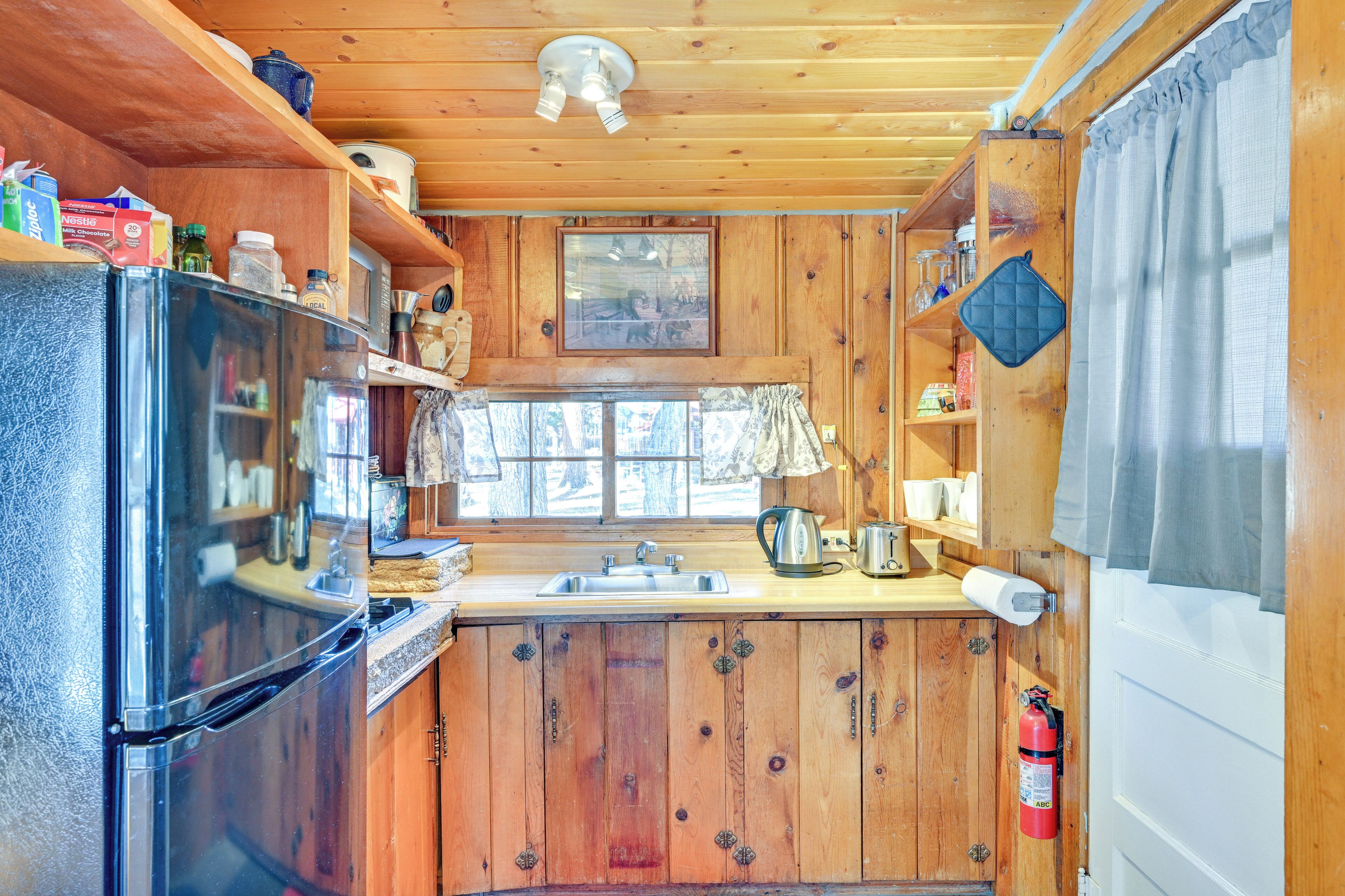 Cocina compacta con armarios de madera, un refrigerador, un lavamanos y una ventana con cortinas.