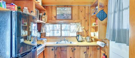 Cocina compacta con armarios de madera, un refrigerador, un lavamanos y una ventana con cortinas.