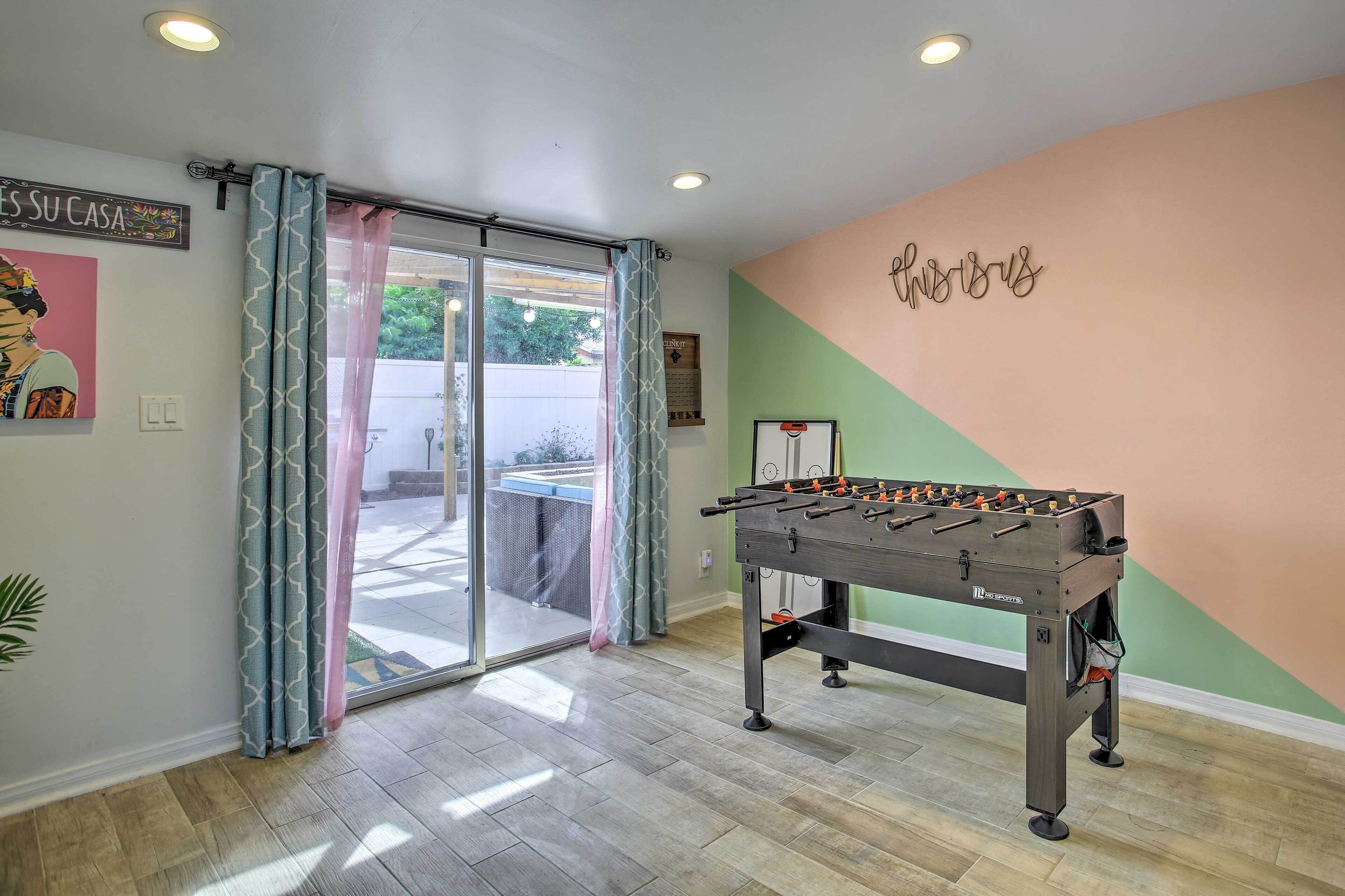 A room with a foosball table, a sliding glass door leading to an outdoor area, and a wall with a motivational quote.