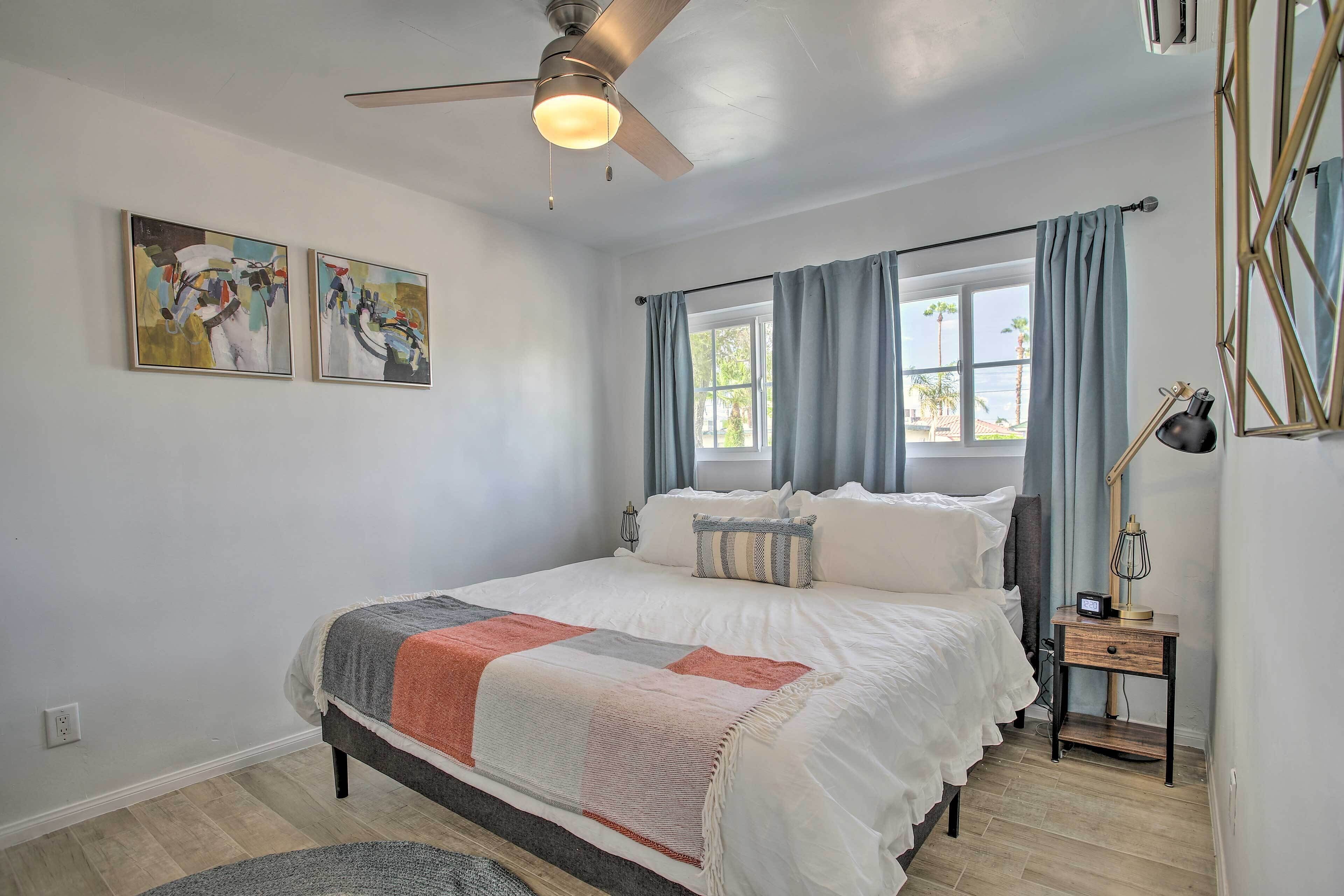 A bedroom with a bed, a nightstand, a ceiling fan, and two abstract paintings on the wall.