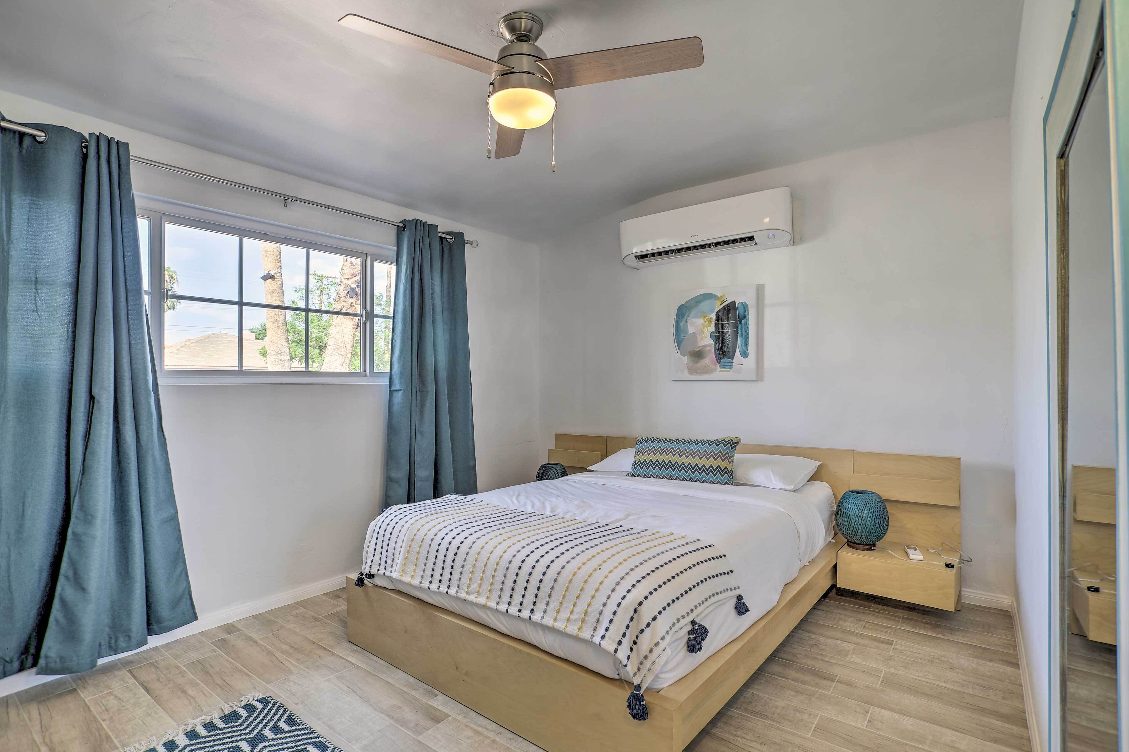 Un dormitorio con cama, ventilador de techo, equipo de aire acondicionado y ventana con cortinas.