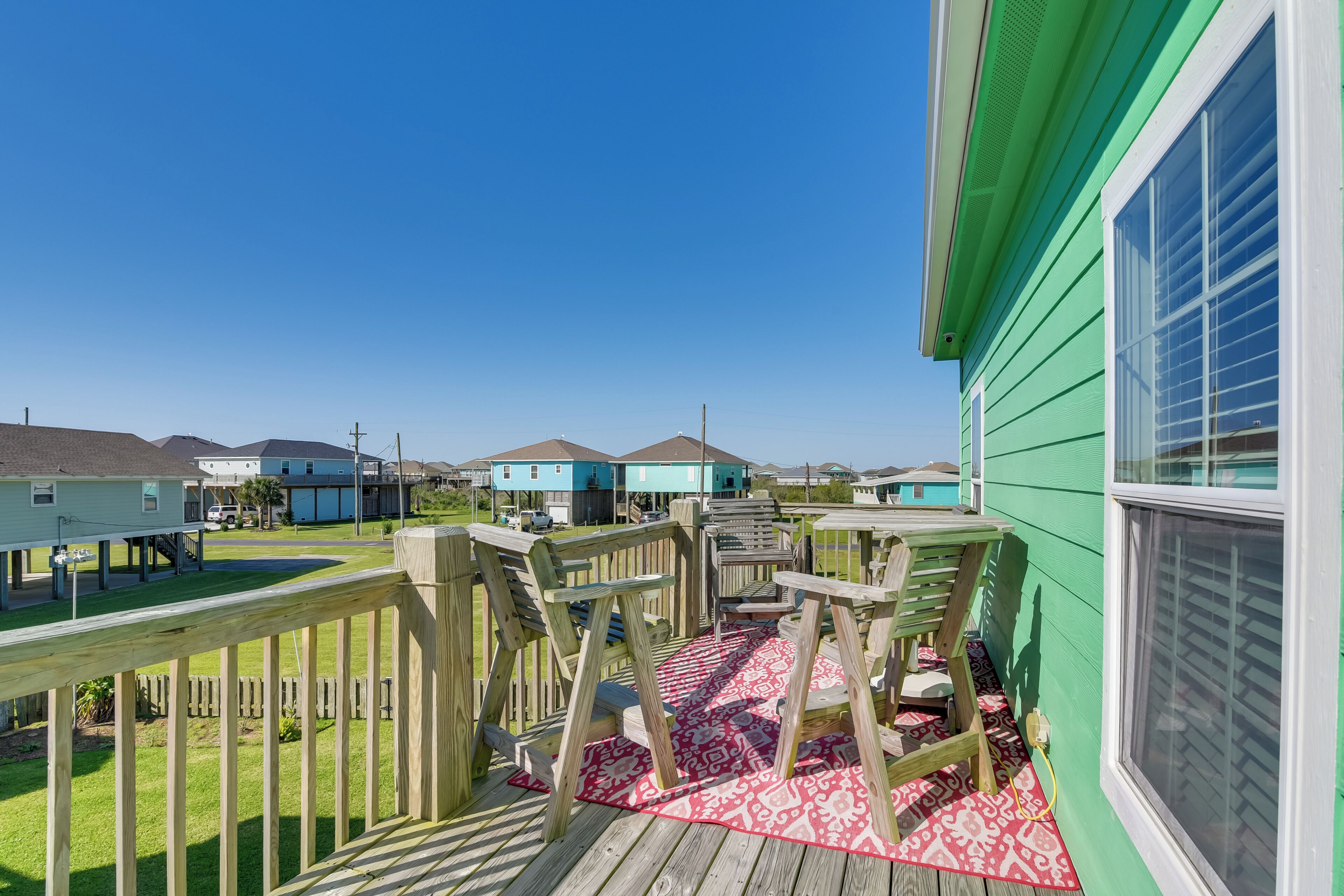 A wooden deck with a red patterned rug, a wooden fence, and a view of neighboring houses.
