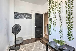 A hallway with a black door, a fan, a rug, and a wall-mounted plant.