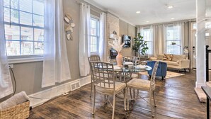 A spacious living room with a dining area, large windows with curtains, a fireplace, and a TV mounted on the wall. - Baltimore Vacation Rental Near Dtwn Towson! (Baltimore)