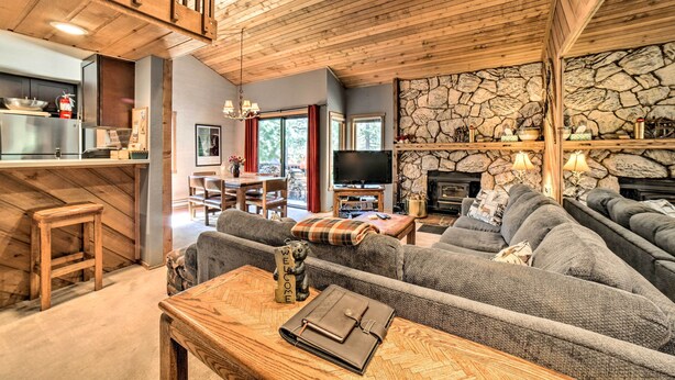 A cozy living room with a stone fireplace, a wooden ceiling, and a modern kitchen area. - Renovated Mammoth Lakes Retreat w/ Private Balcony (Mammoth Lakes)