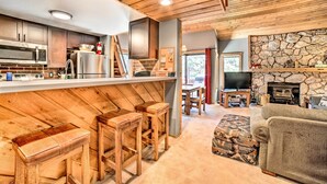 A modern kitchen with wooden accents, a stone fireplace, and a cozy seating area with a television. - Renovated Mammoth Lakes Retreat w/ Private Balcony (Mammoth Lakes)