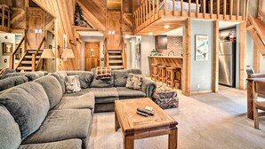 A spacious living area with a large sectional sofa, a wooden coffee table, and a kitchen area with a refrigerator and bar stools. - Renovated Mammoth Lakes Retreat w/ Private Balcony (Mammoth Lakes)