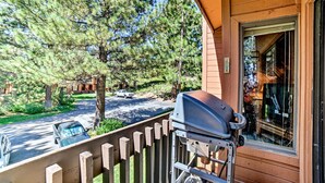 A wooden house with a barbecue grill on the porch, a view of a road with parked cars, and a large tree in the background. - Renovated Mammoth Lakes Retreat w/ Private Balcony (Mammoth Lakes)