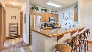 Une cuisine moderne avec des meubles en bois, des appareils en acier inoxydable, un îlot central doté de tabourets et agrémentée de plantes décoratives.