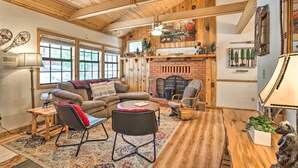 A cozy living room with a fireplace, wooden ceiling beams, a sofa, a coffee table, and a rug.