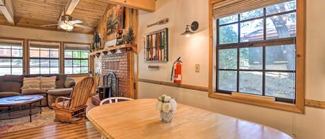 A cozy living room with a wooden dining table, a fireplace, and a large window.