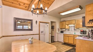 A kitchen with wooden cabinets, a dining table with chairs, a chandelier, and a refrigerator.