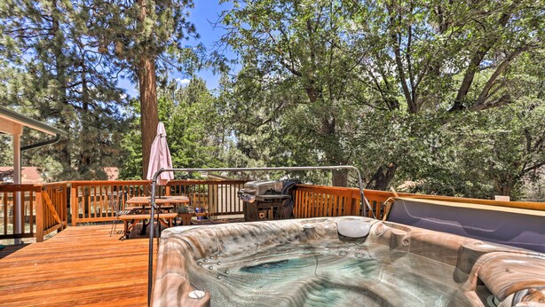 A hot tub on a wooden deck with a table and chairs, surrounded by trees.