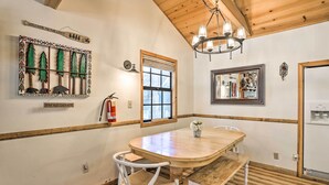 A dining area with a wooden table and chairs, a chandelier, a wall-mounted mirror, and a window with blinds.