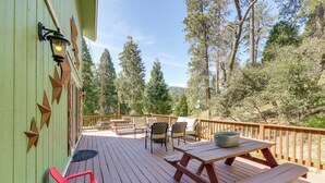 Une terrasse en bois, agrémentée de tables et de chaises pour pique-nique, entourée d’une balustrade en bois, et offrant une vue sur une zone boisée.