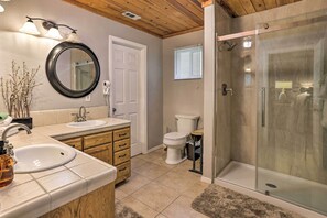 A bathroom with a double sink, a toilet, a glass-enclosed shower, and a mirror with lights. - Remodeled Crestline Retreat: Walk to Lake Gregory! (Crestline)