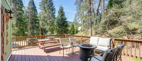 A wooden deck with outdoor furniture, including chairs and a table, surrounded by trees.