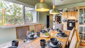 A dining area with a wooden table set for a meal, surrounded by chairs, and a kitchen in the background. - Group Friendly! Gem 5 Mi to Joshua Tree Nat'l Park (Joshua Tree)