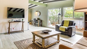A spacious living room with a flat-screen TV mounted on the wall, a wooden coffee table, a leather sofa, and a dining area with a table and chairs. - Group Friendly! Gem 5 Mi to Joshua Tree Nat'l Park (Joshua Tree)