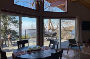 A dining area with a table set for four, large sliding glass doors leading to an outdoor patio with a grill and seating. - Secluded Home on 1-acre Lot w/ Unparalleled Views (Skyforest)