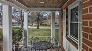 A covered patio with a metal table and chairs, brick walls, and a view of the neighborhood.