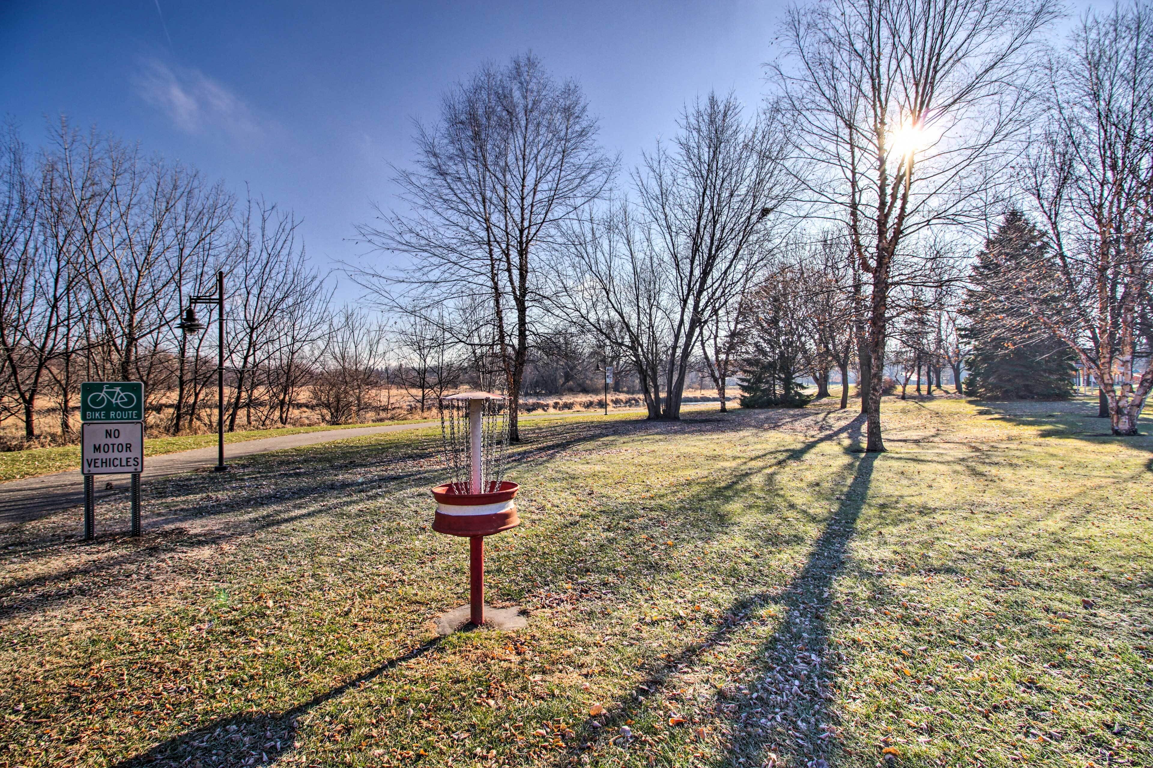 A park with a bike route sign, a disc golf basket, and leaf-covered ground.