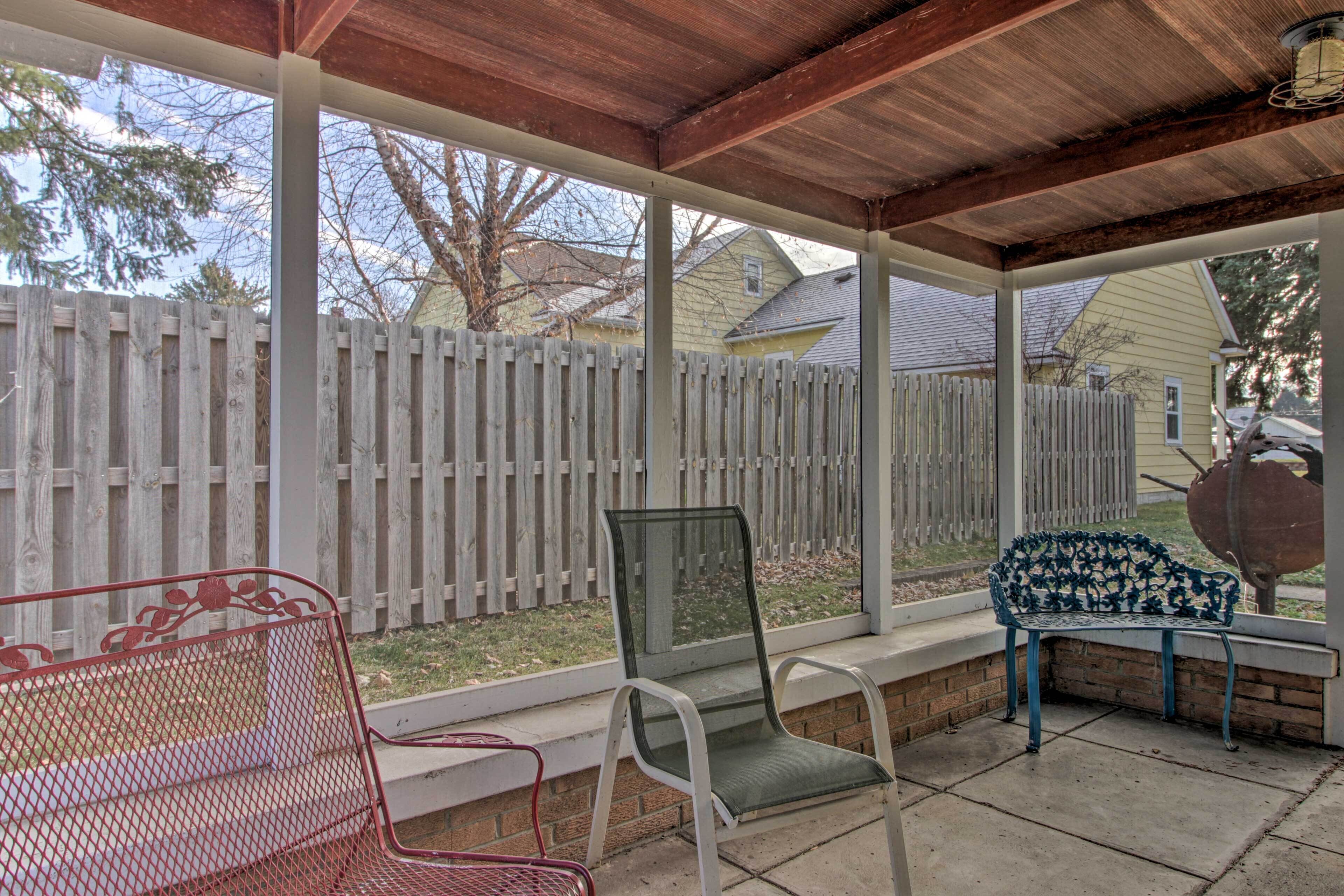 A covered patio with a wooden ceiling, a white fence, and a bench.
